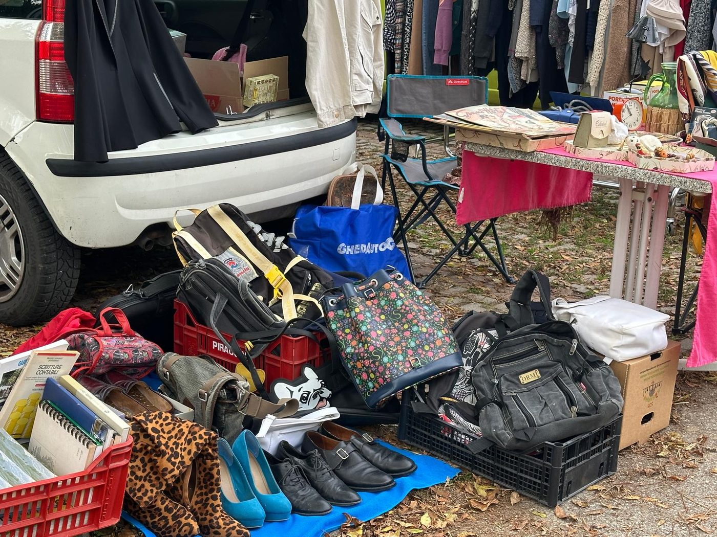 Borse, zaini, scarpe e libri in cassette di plastica davanti a un bagagliaio aperto