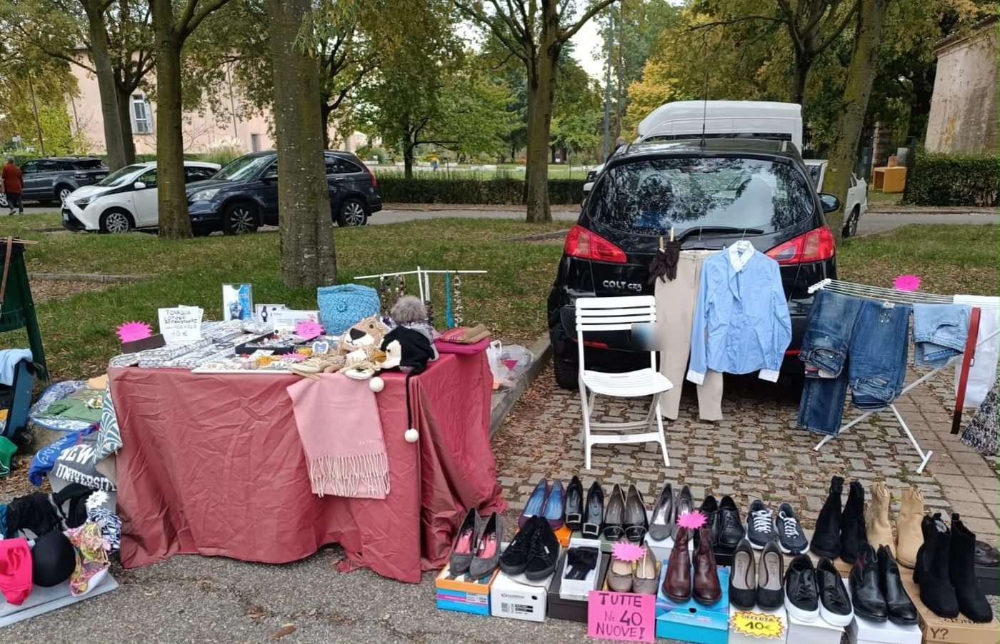Una fila di scarpe davanti al bagagliaio, camicie appese e uno stendino di jeans, con il parco sullo sfondo